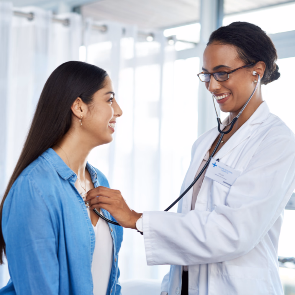 Female doctor using a stethoscope to examine a smiling patient during a medical consultation.