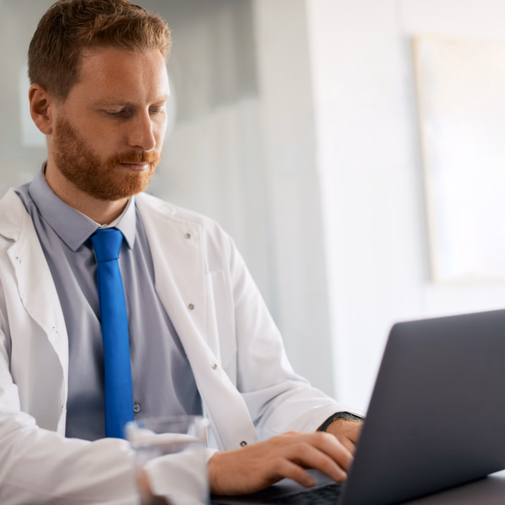 Male physician reviewing patient information on a laptop in a medical office