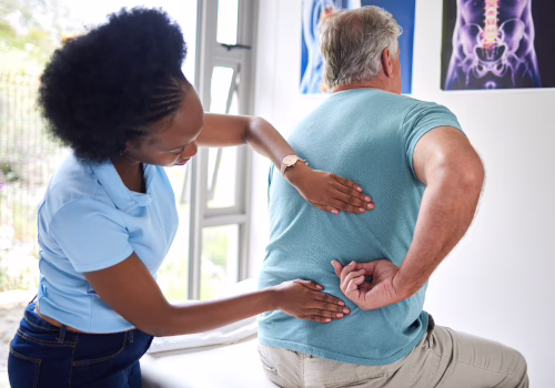 Healthcare provider examining an older man's back during a pain management assessment