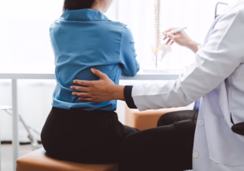 Healthcare professional examining a patient's lower back during a medical appointment in Dallas, TX
